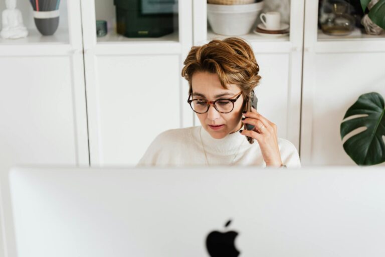 serious lady talking on cellphone while sitting near computer