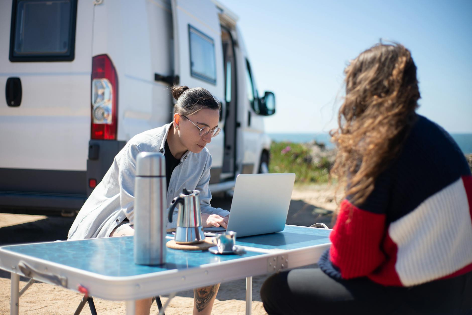 a man sitting at a table using a laptop near a motorhome